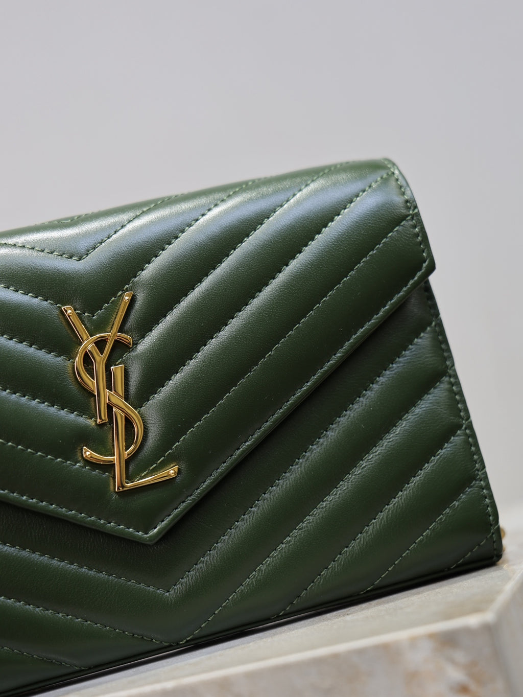 Green leather clutch flap with YSL gold-tone logo and quilted chevron stitching.