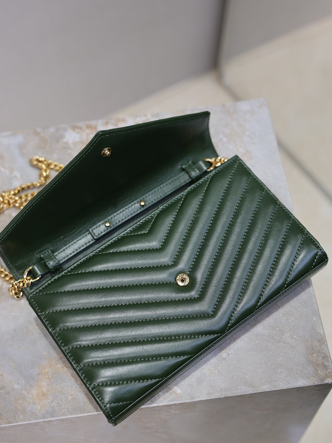 Green quilted leather clutch opened with black interior lining, snap closure, and YSL logo.