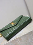 Green quilted leather clutch with YSL gold-tone logo and fold-over top flap, side view.