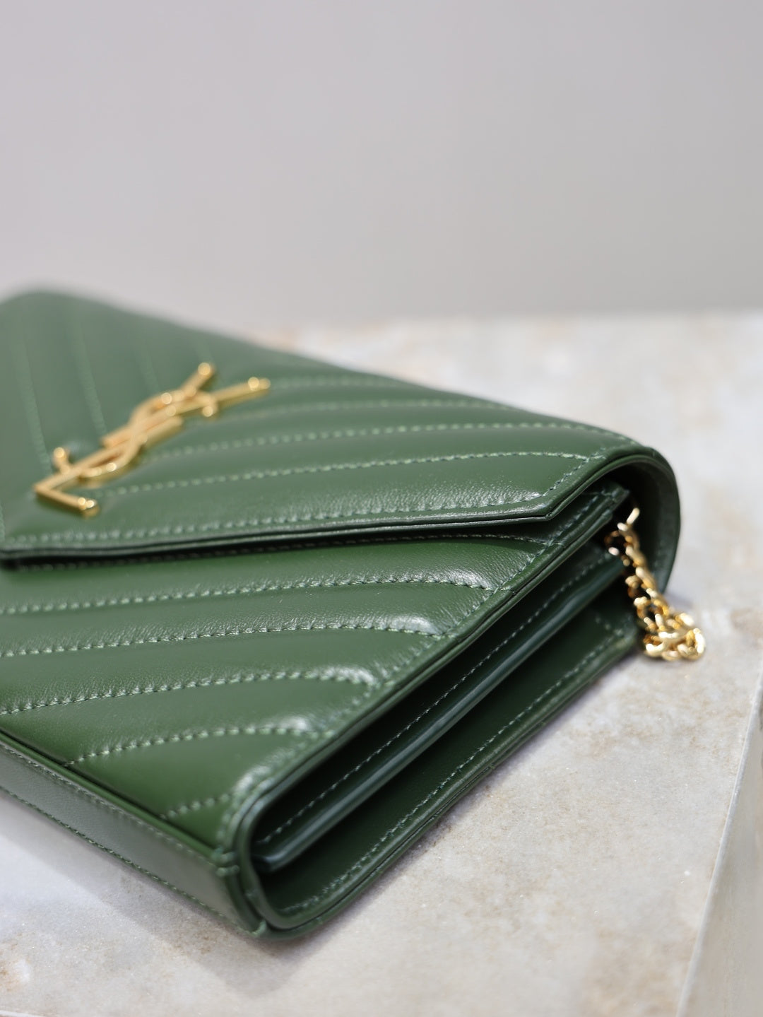 Green quilted leather clutch opened, showing black lining and gold-tone interior hardware.