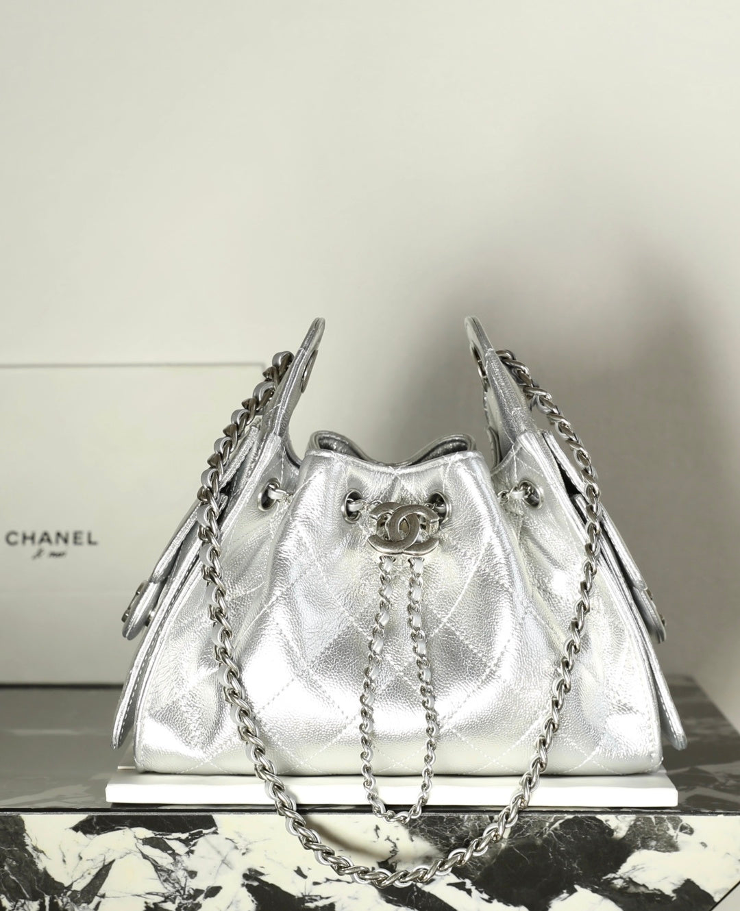 Silver quilted drawstring handbag with chain handles and metal ring hardware