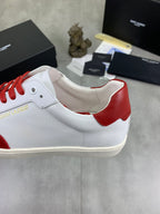 White sneaker with red heel panel and red lace-up, cream sole.