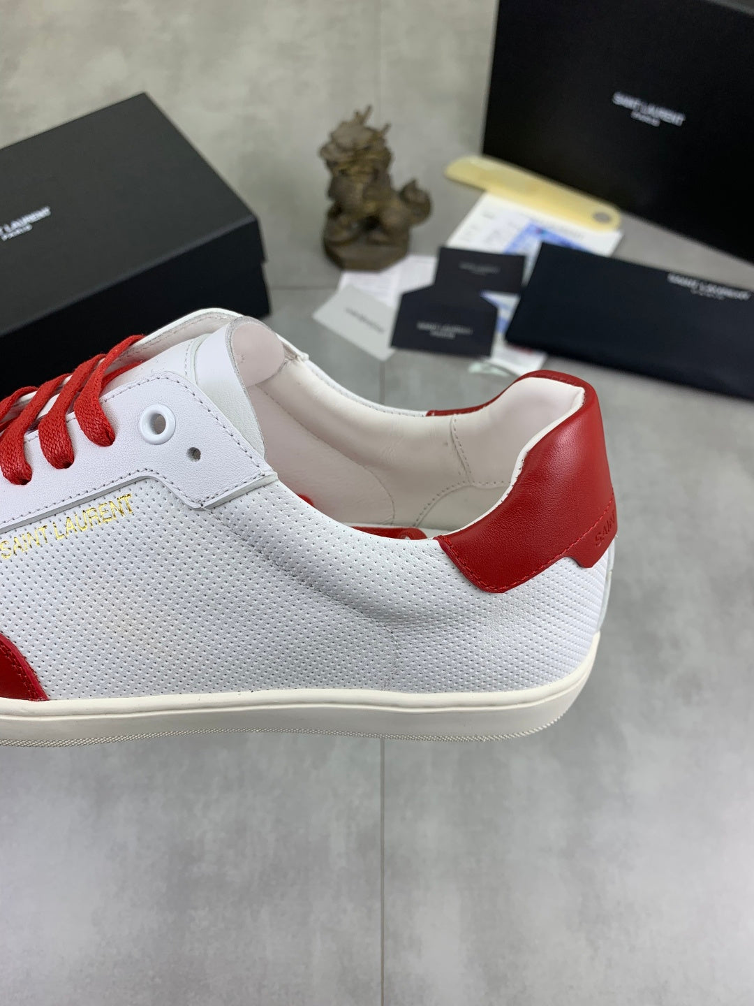 White sneaker with red heel panel and red lace-up, cream sole.