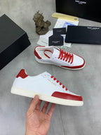White and red low-top sneakers with red laces and cream midsole, held in hand.