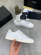White lace-up sneakers held in hand, textured upper and beige rubber sole