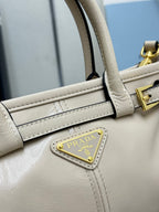 Cream leather Prada handbag detail with side strap, gold-tone hardware, and logo plaque