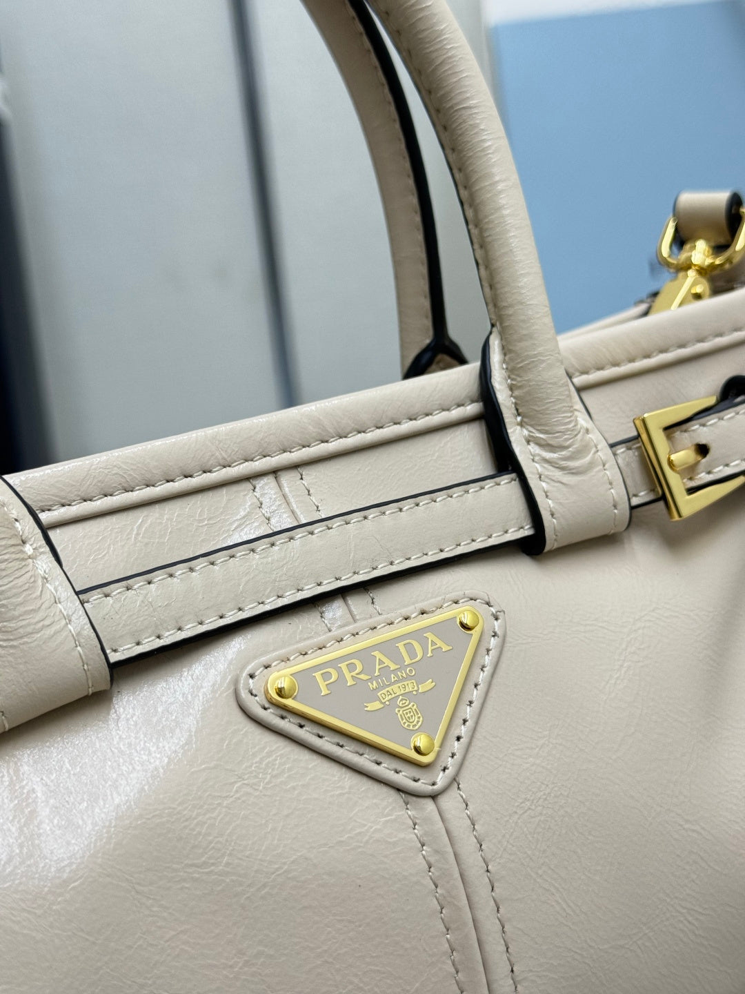 Cream leather Prada handbag detail with side strap, gold-tone hardware, and logo plaque