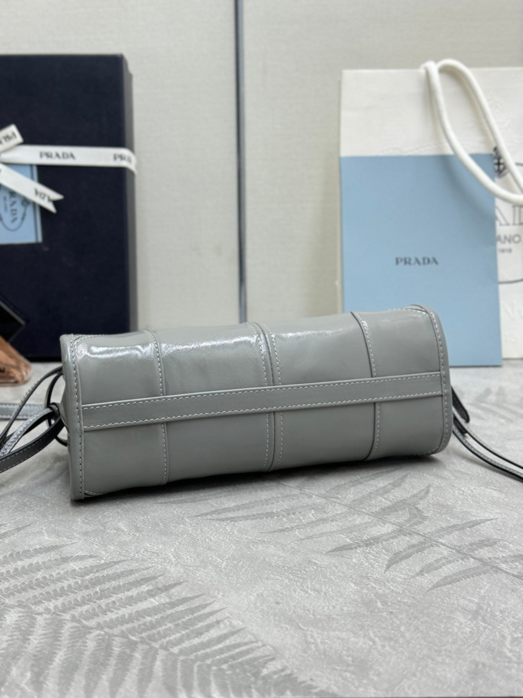 Light gray leather clutch-style handbag with rolled top, foldover flap, and shoulder strap