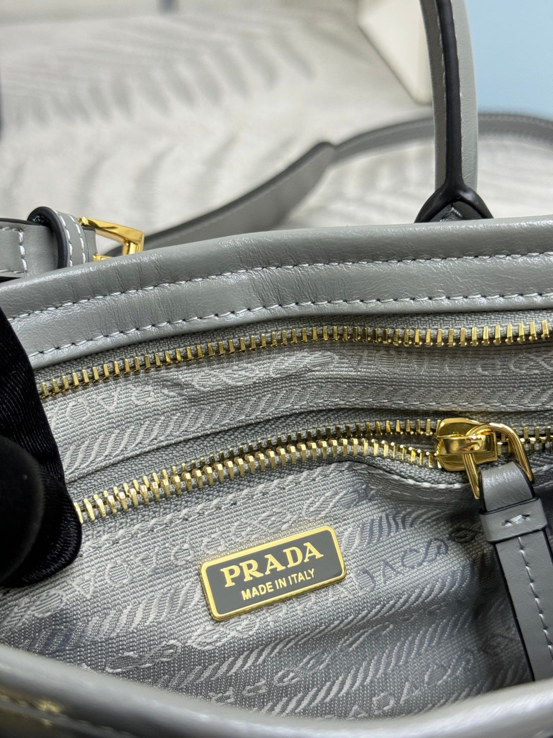 Light gray leather handbag close-up with double zippers and PRADA logo patch inside