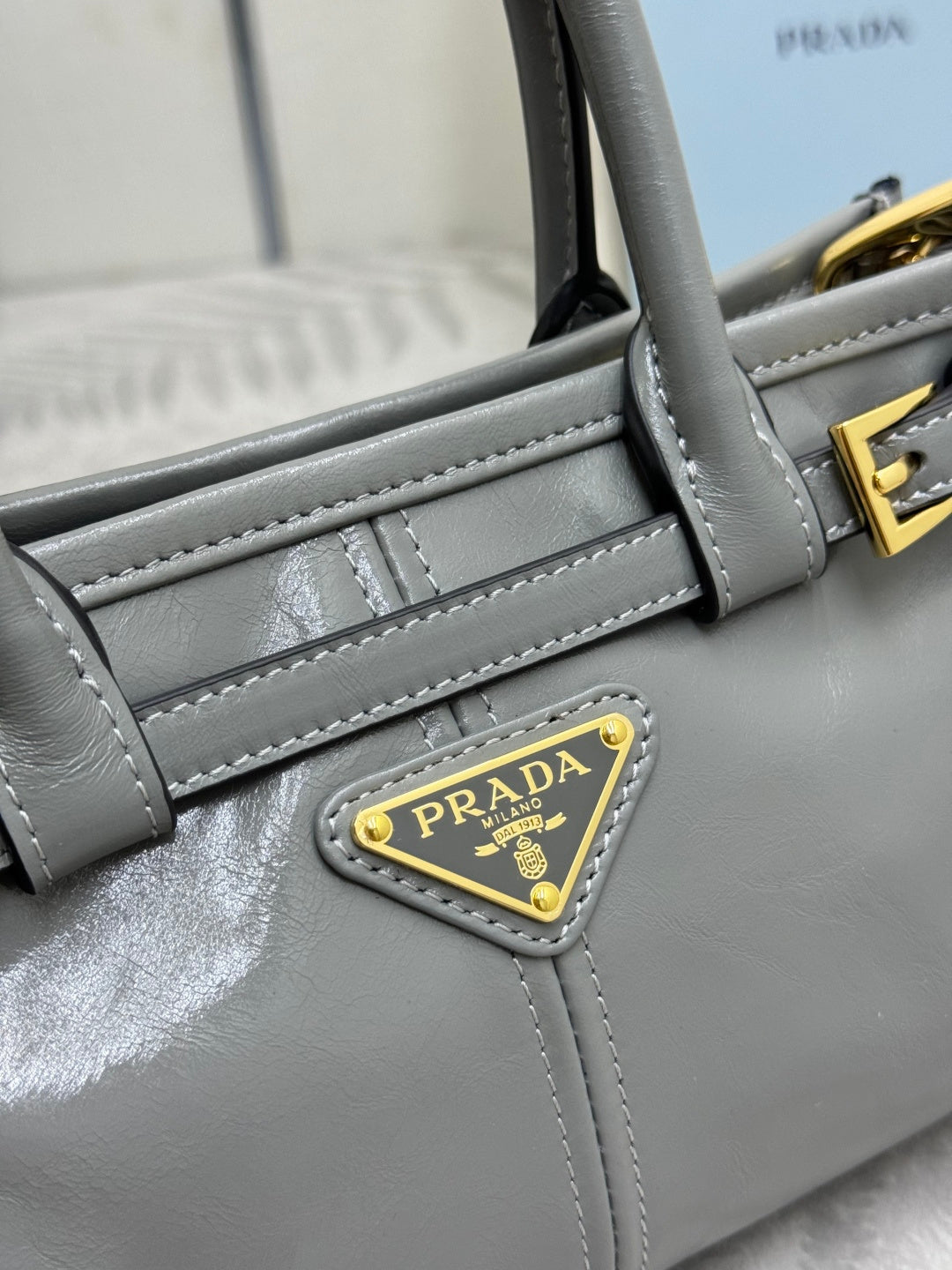 Light gray leather handbag side panel with stitched trim and PRADA logo plaque