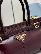 Burgundy leather handbag with top handles and triangular Prada logo plaque, gold hardware.