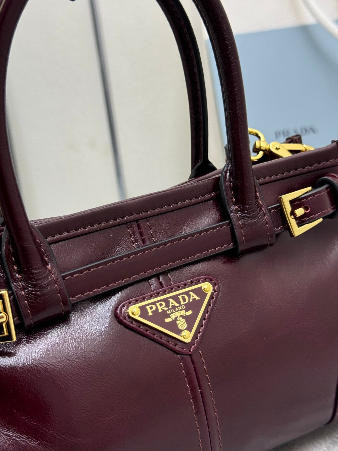 Burgundy leather handbag with top handles and triangular Prada logo plaque, gold hardware.