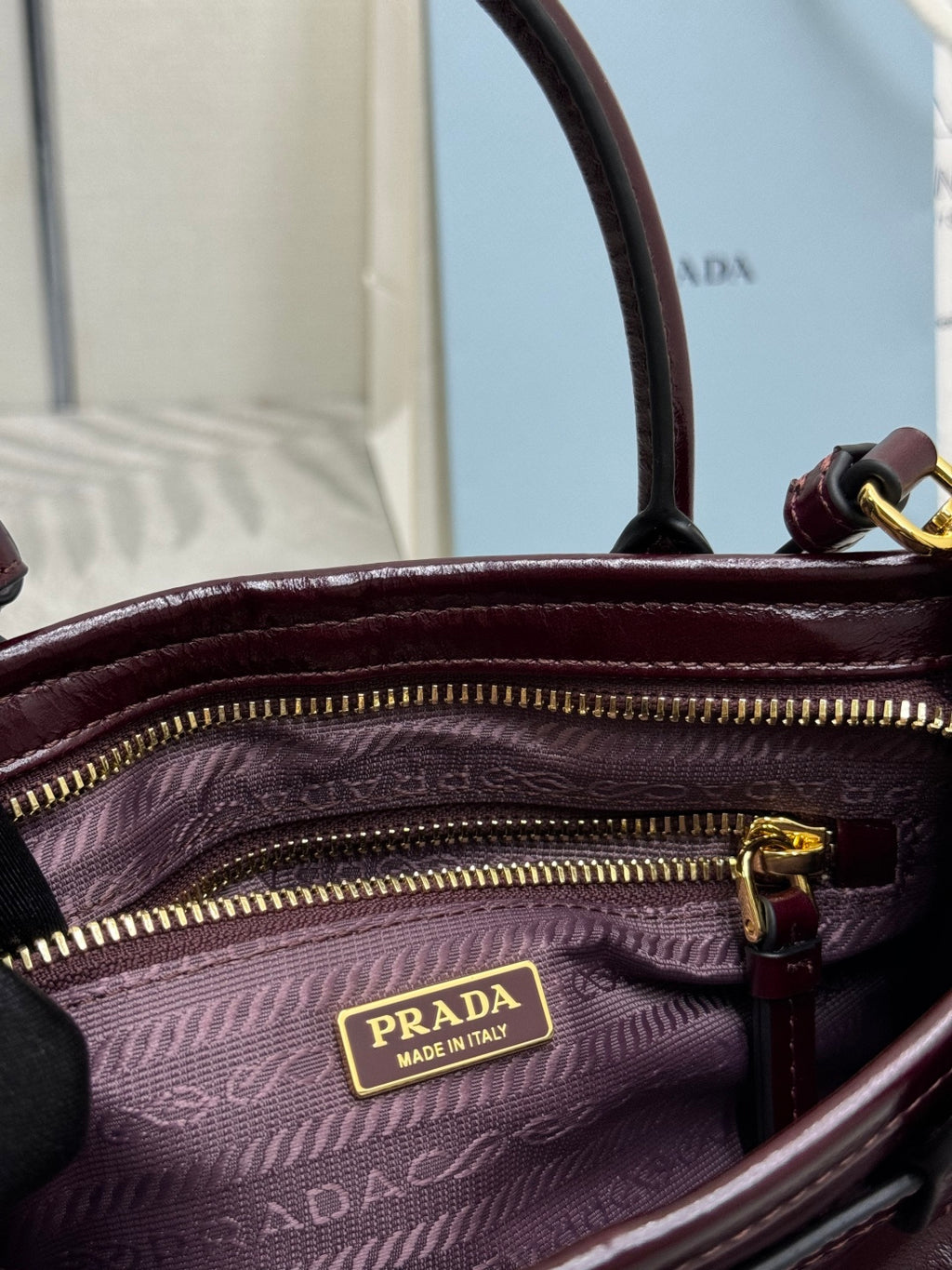 Burgundy leather handbag with zip pocket and Prada logo patch on patterned lining.