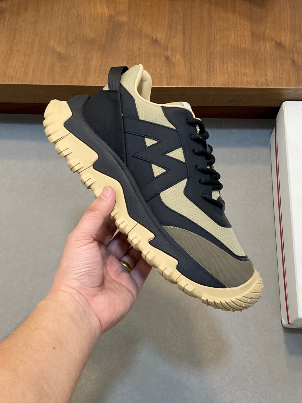 Moncler sneakers held in hand; dark navy upper with beige accents and lace-up closure