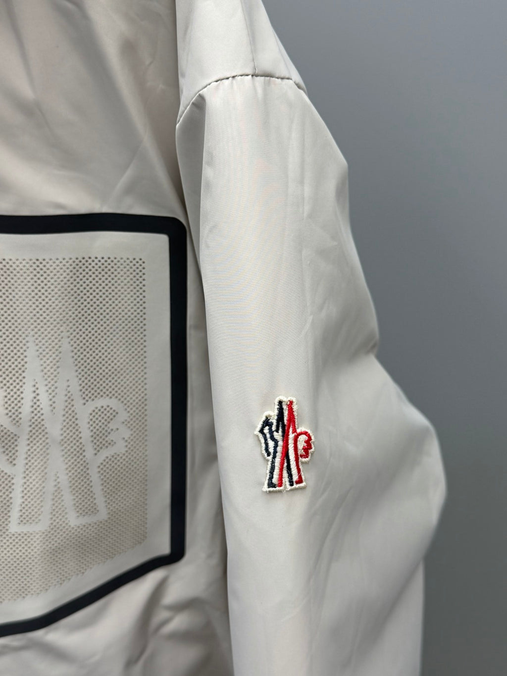 White-beige long puffer jacket sleeve with red-blue logo patch detail
