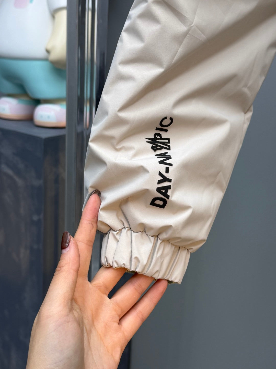 Light beige puffer jacket sleeve cuff with vertical "DAYANAY" text