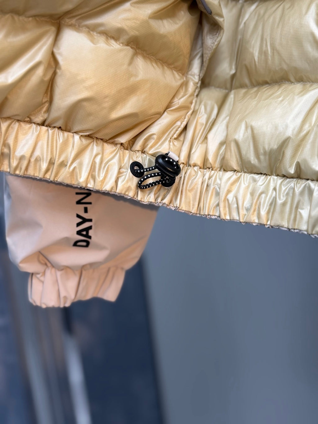 Light beige puffer jacket lower hem with quilted padding and "DAYANAY" label