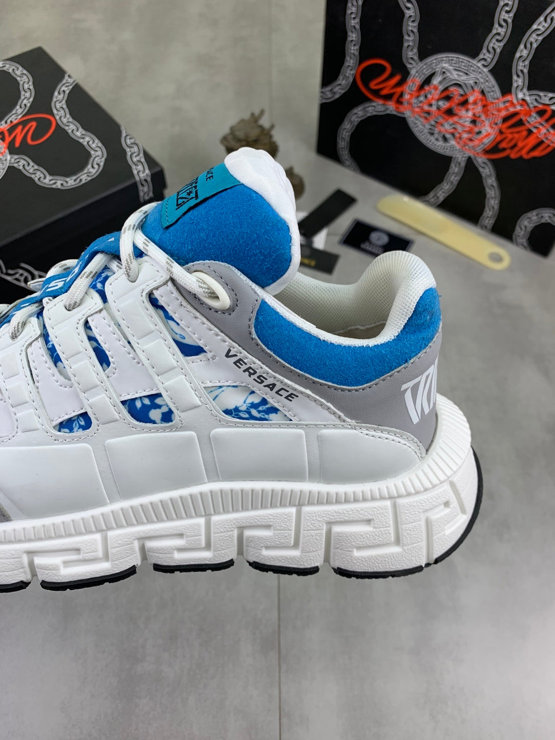 White sneaker with blue panel trim, blue laces, and chunky tread sole.