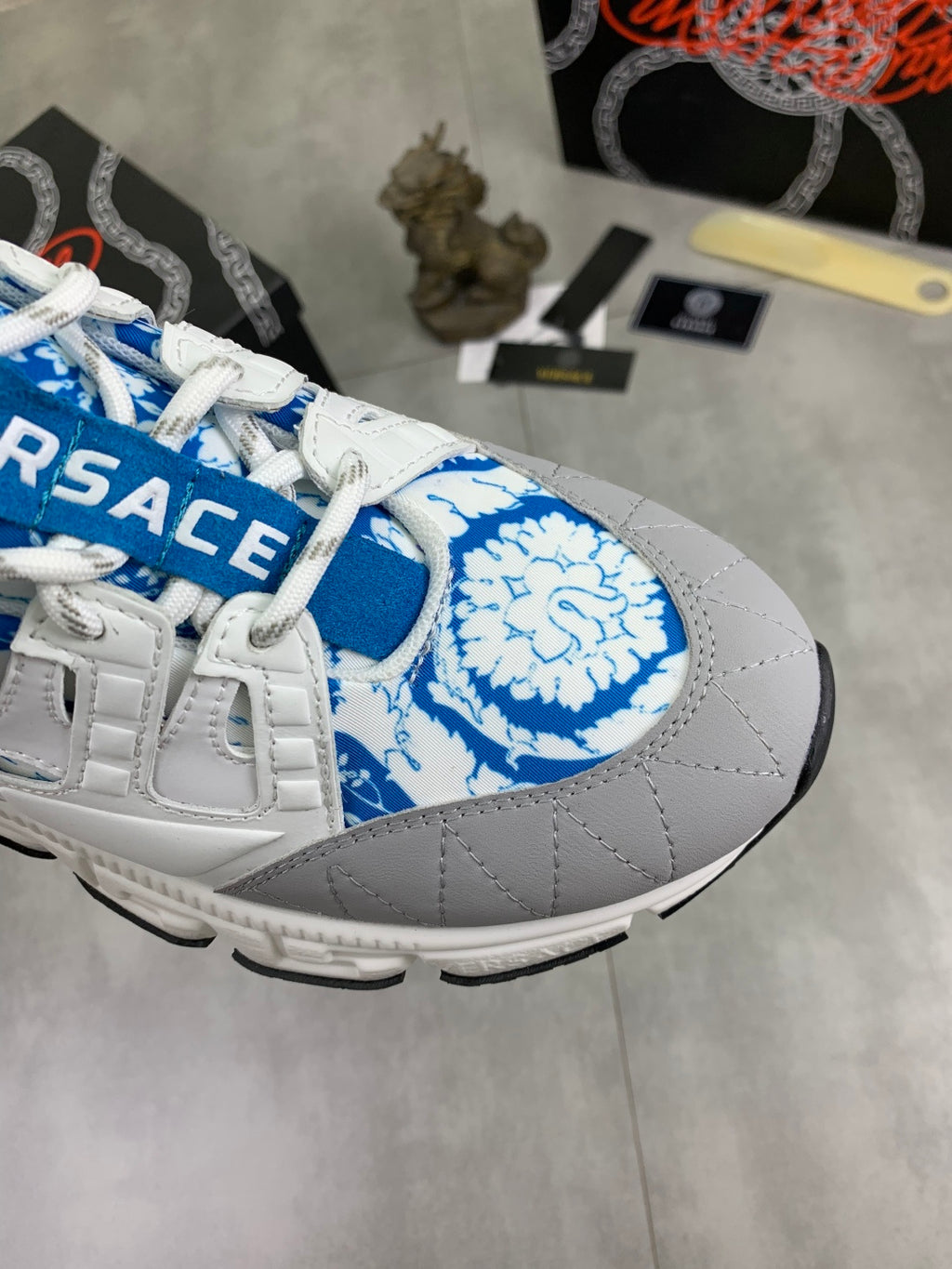 White sneaker with blue printed logo patch, blue laces, and padded collar.