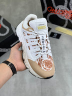 White and tan low-top sneakers with brown floral detail on the toe and side
