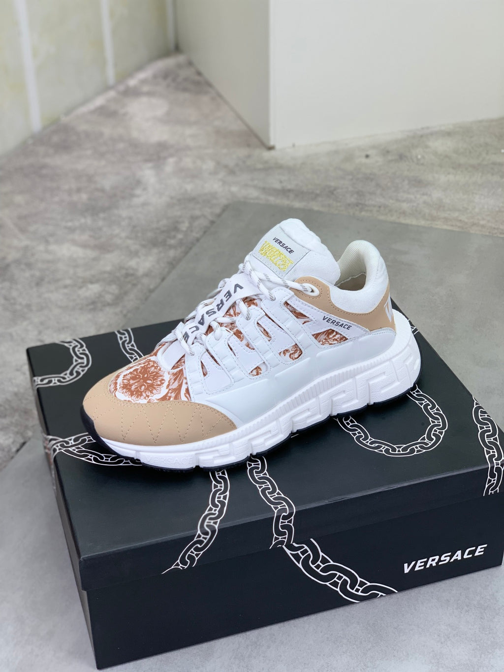 White and tan low-top sneakers with brown floral toe panel on black box