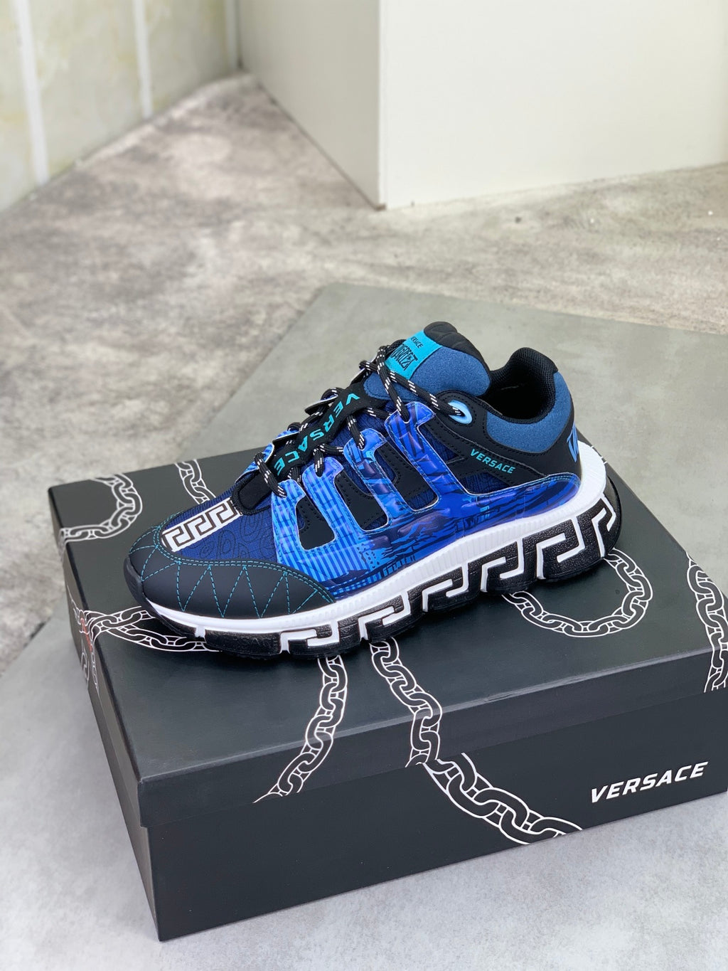 Blue Versace sneakers on a box, with white midsole and bold Greek key side emblem