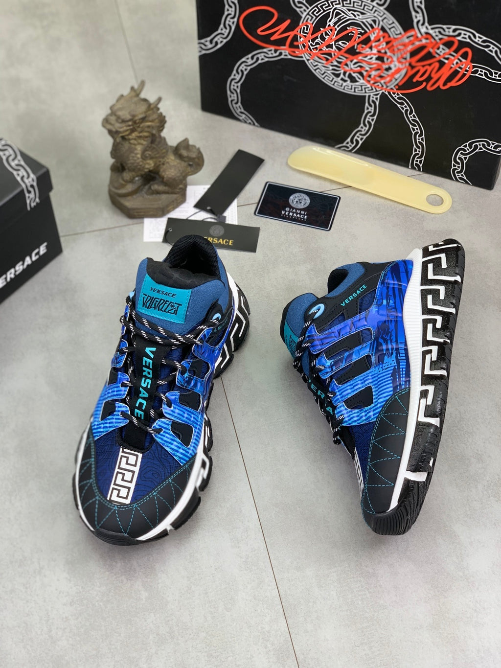 Blue and black Versace sneakers viewed from side, showing Velcro straps and Greek key logo