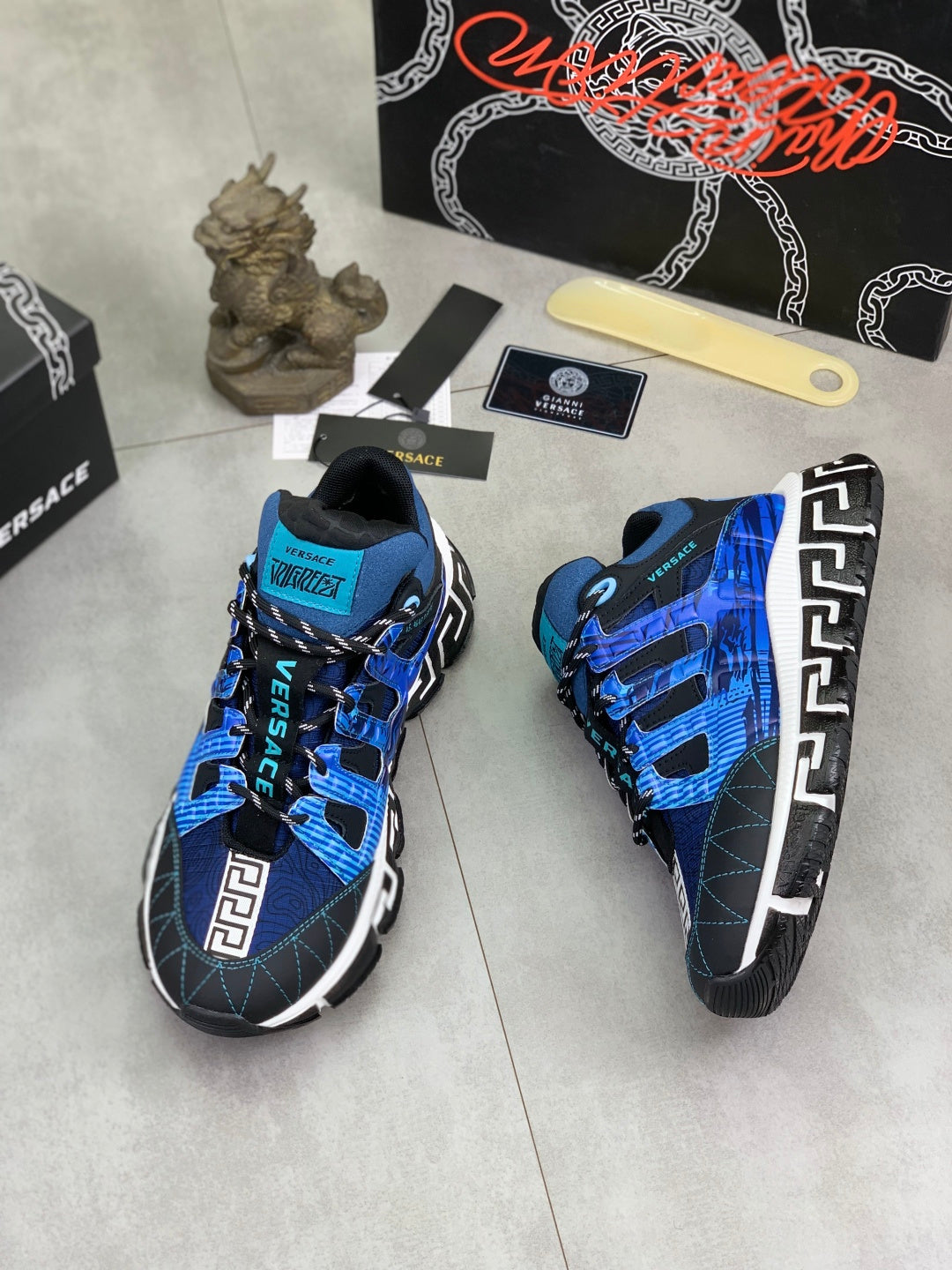Blue and black Versace sneakers viewed from side, showing Velcro straps and Greek key logo