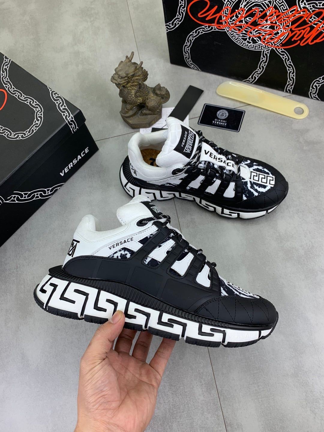 Two black and white sneakers with white laces and Greca-style side trim