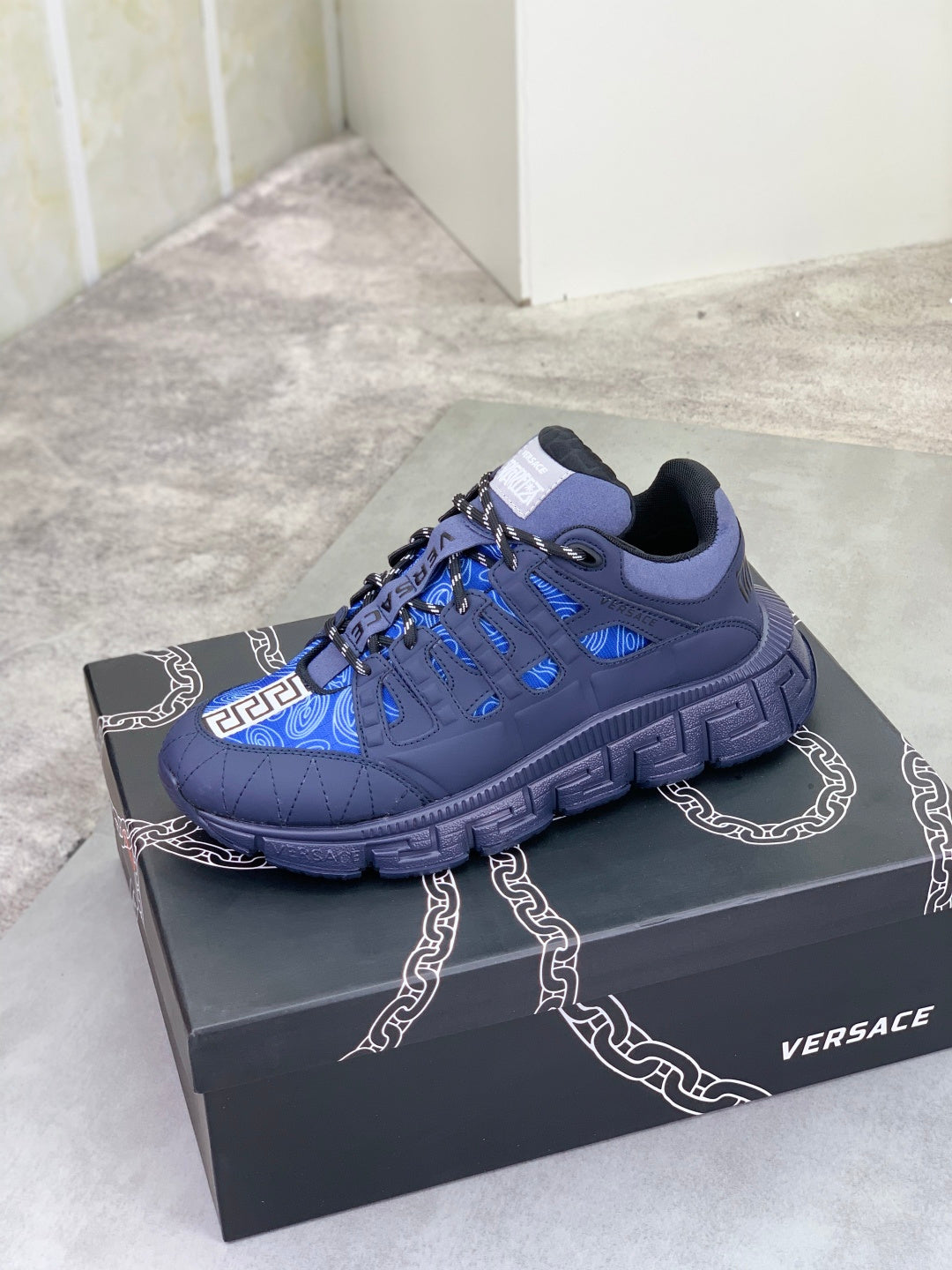 Versace luxury sneaker on box, dark navy with blue geometric stripe upper