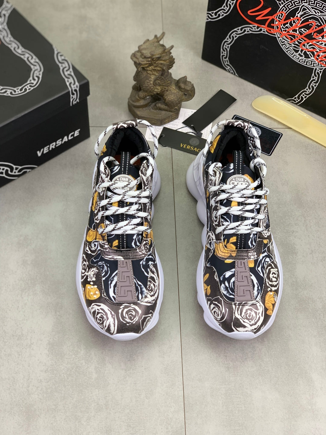 Versace printed sneakers pair, black-and-white graphic with yellow accents, white soles.