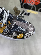 Close-up of printed sneaker upper with gold Greek-key logo, black-and-white graphic and lace.