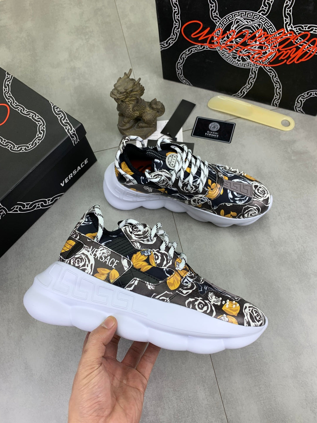 Printed lace-up sneakers held in hand, black-and-white pattern with yellow accents and white soles.