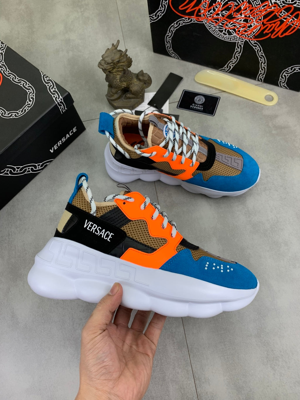 Versace chunky sneakers held in hand, blue orange black uppers with white sole