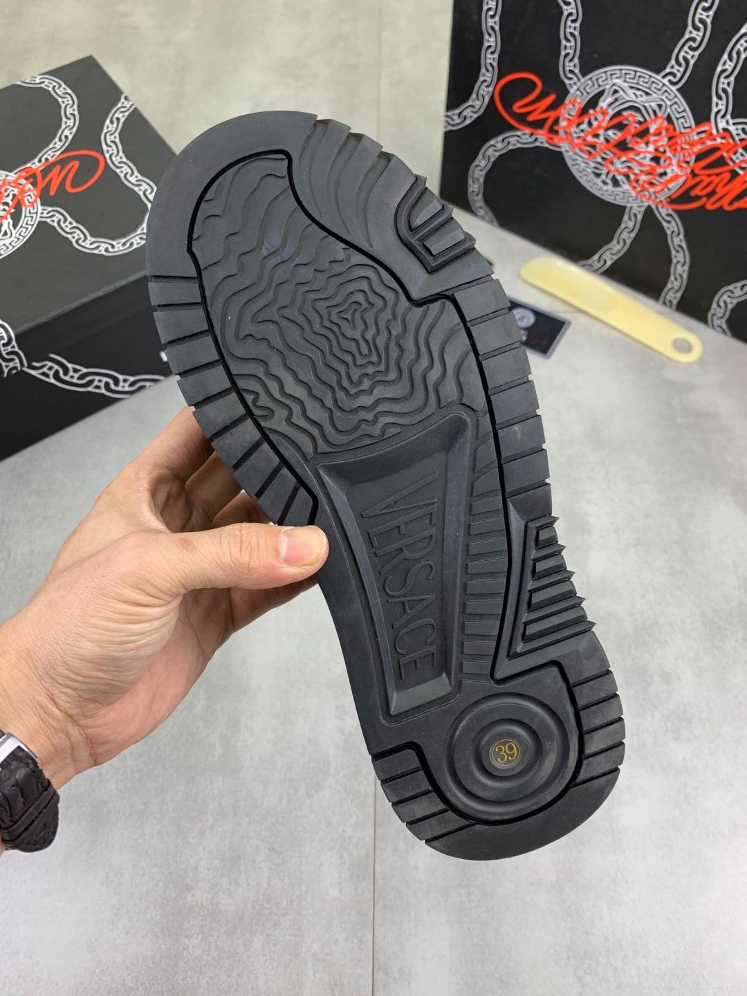 Luxury Versace dark gray sneaker outsole view with rugged tread and circular logo.