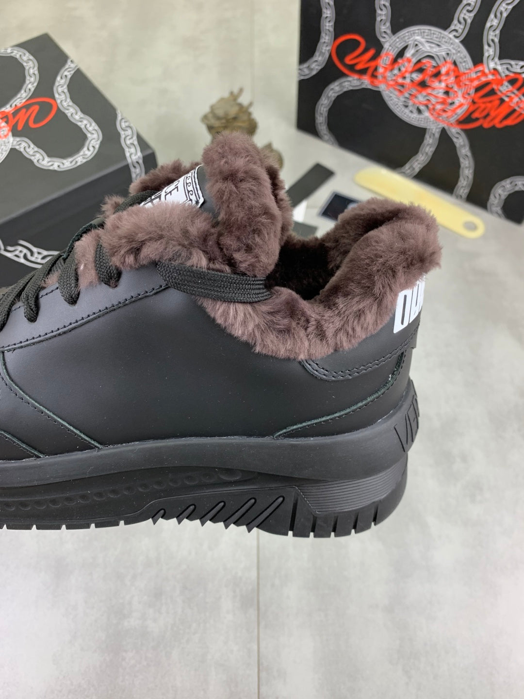 Luxury Versace dark gray sneaker close-up with taupe faux-fur collar detail and laces.