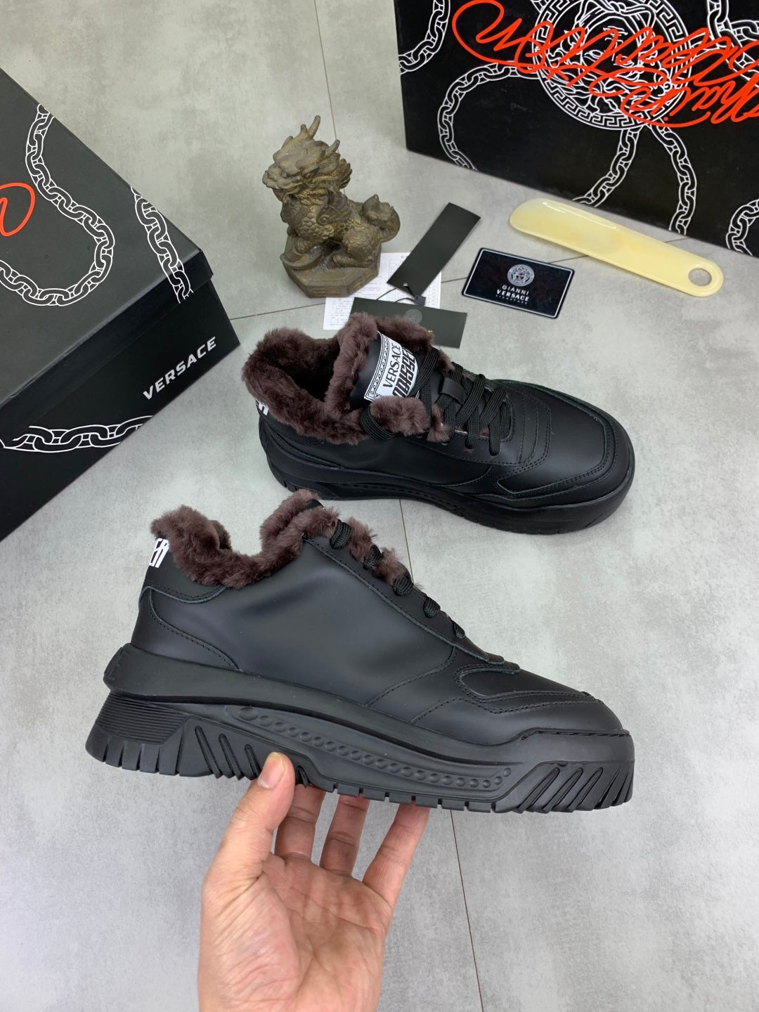 Luxury Versace dark gray sneakers with taupe faux-fur collar, lace-up fit, and thick tread.
