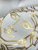 White fabric close-up with repeating gold Medusa face pattern