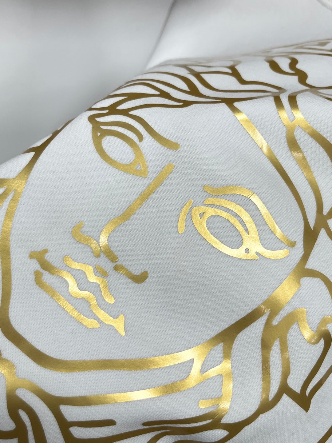 White fabric close-up with repeating gold Medusa face pattern
