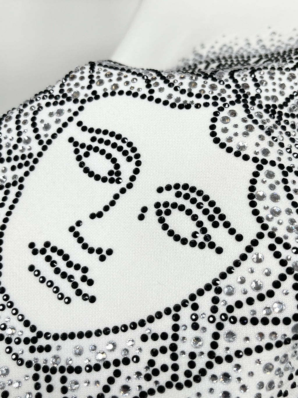 White sweatshirt with studded Medusa-style face graphic, close-up