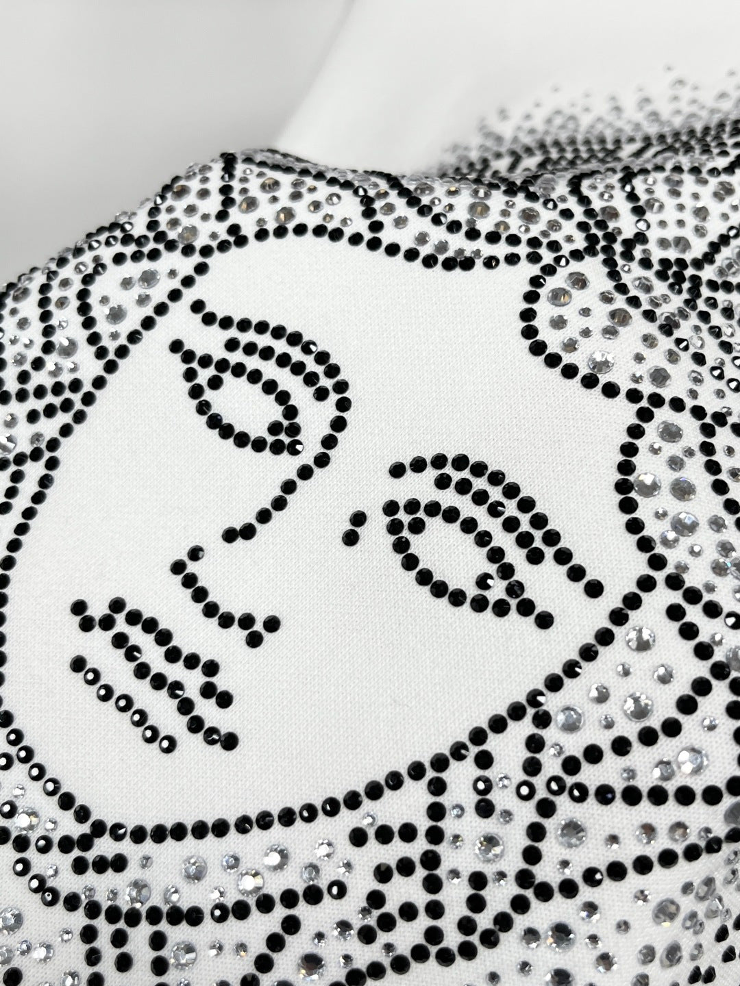 White sweatshirt with studded Medusa-style face graphic, close-up