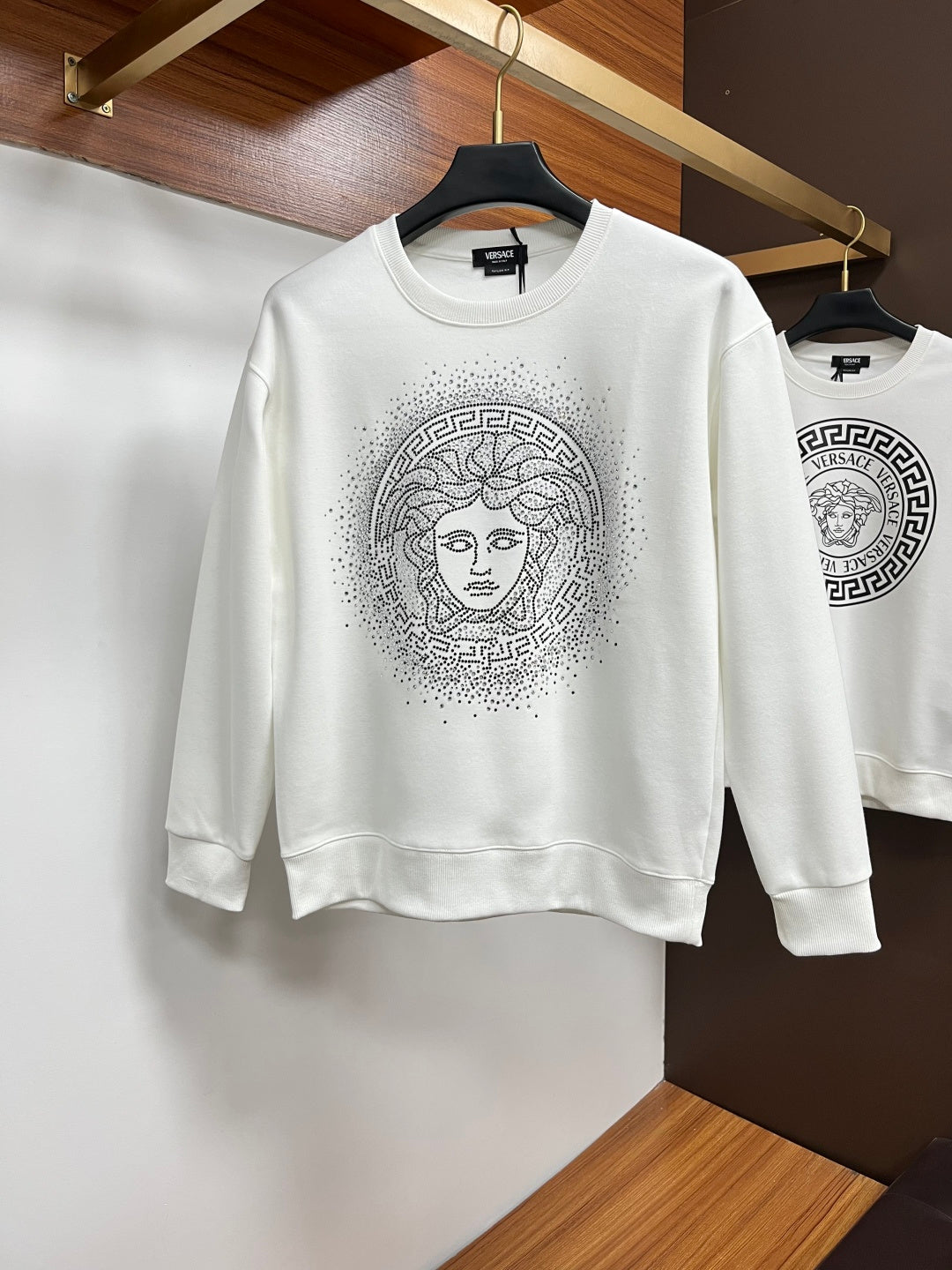 White crewneck sweatshirt with studded Medusa-style face graphic on the chest