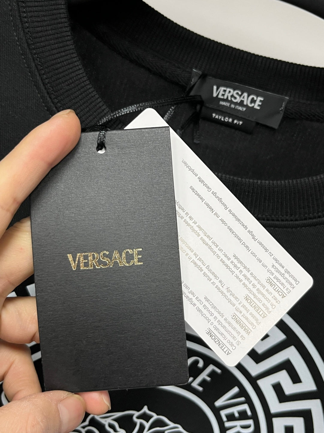 Black crewneck sweatshirt collar with attached Versace hang tag