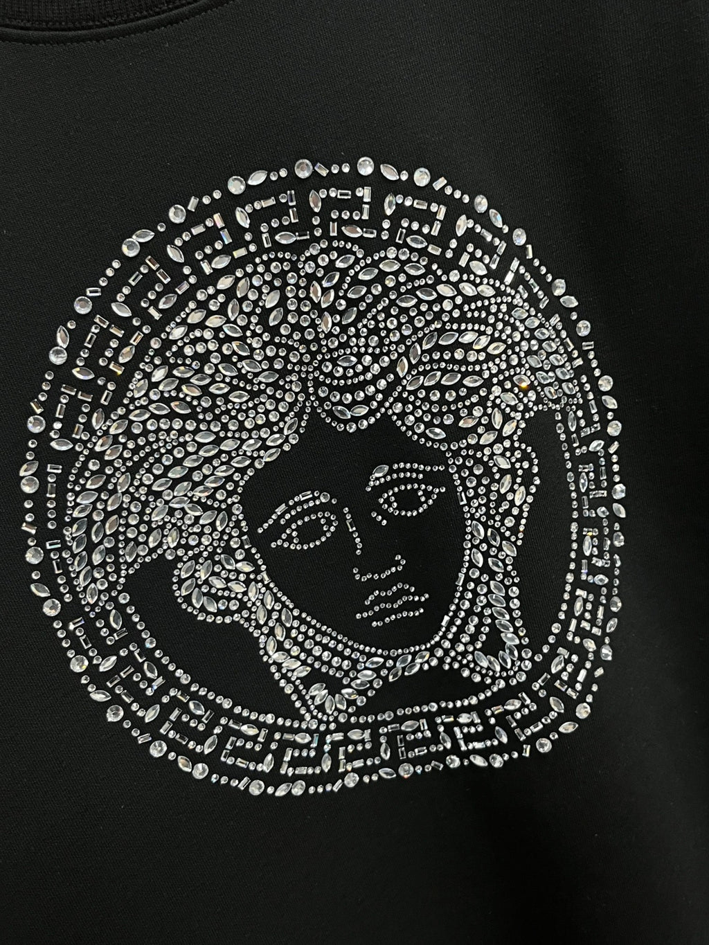Black crewneck sweatshirt with detailed jeweled face emblem graphic