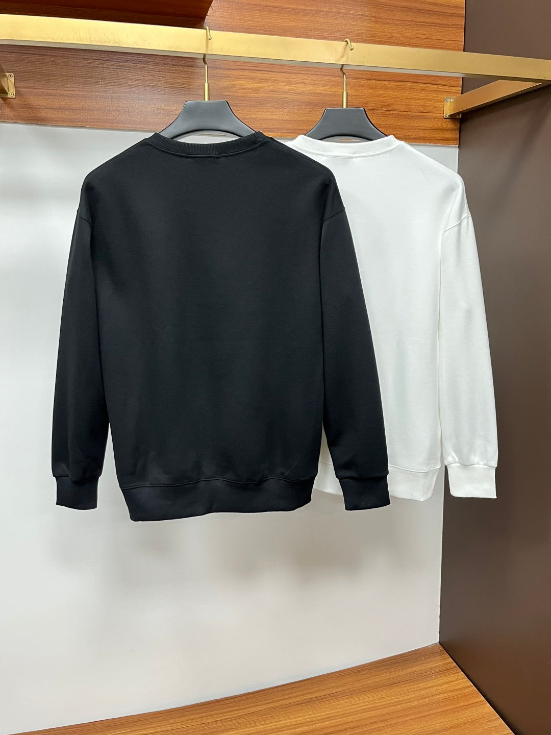 Black and white crewneck sweatshirts hanging, back view