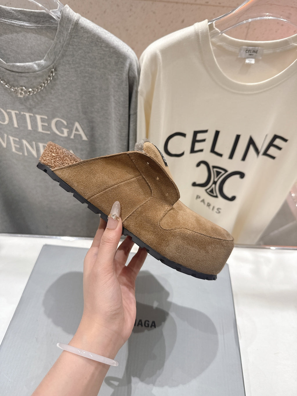 Brown suede slip-on sandal with shearling lining, held in hand, side view