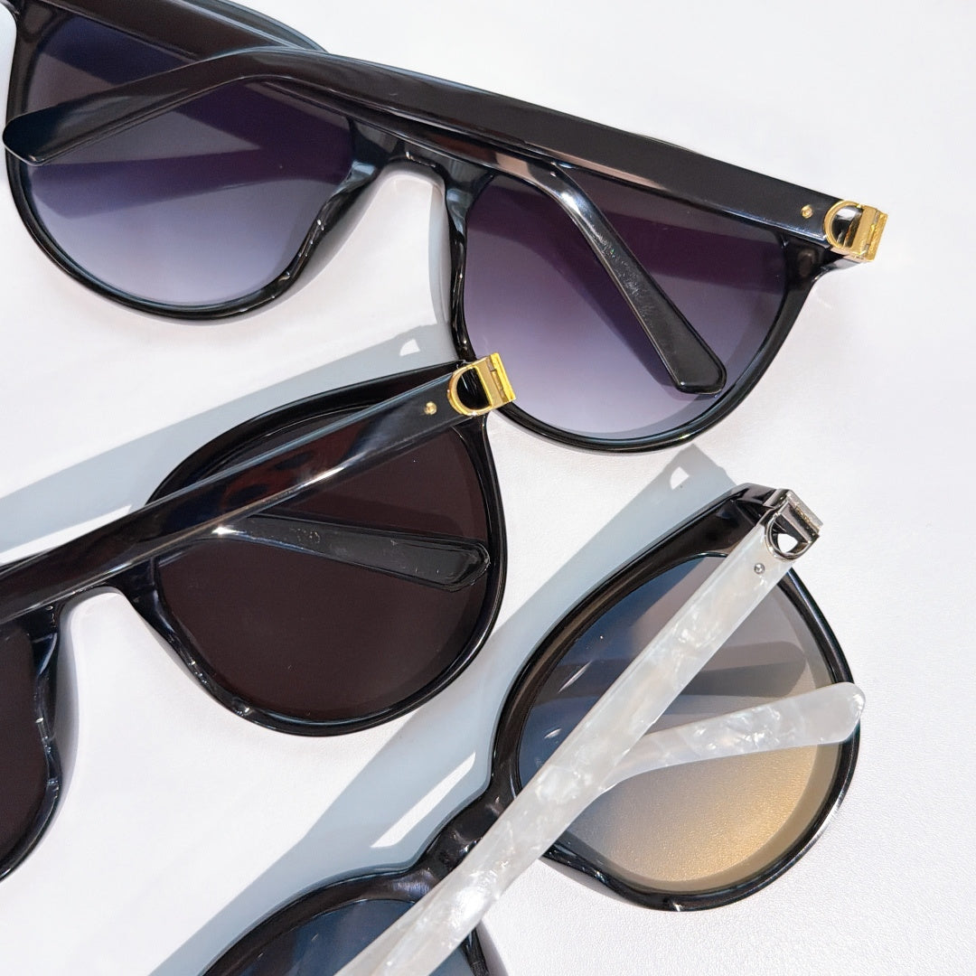 Sunglasses close-up with black frames and dark lenses, gold hinge details visible