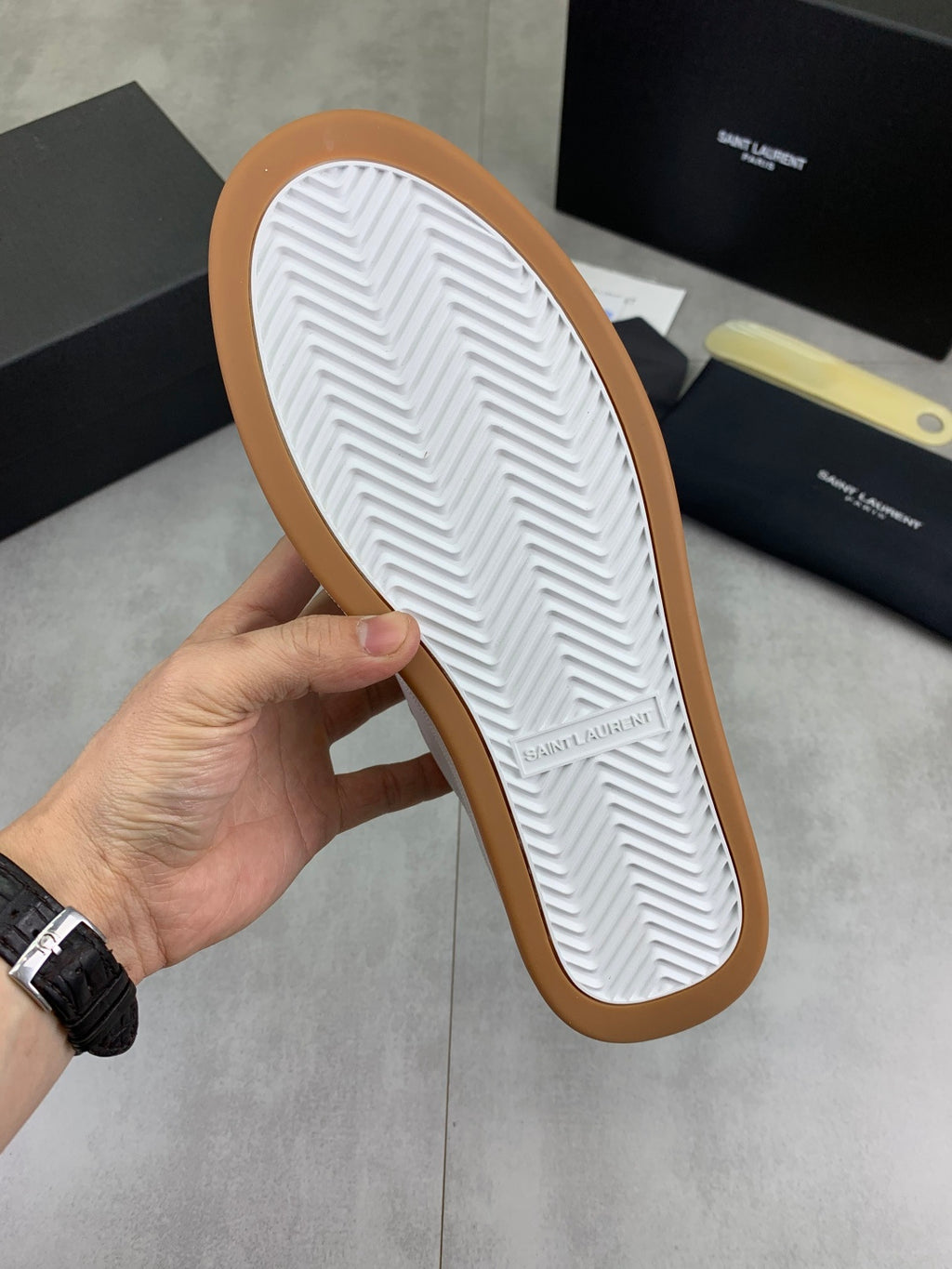 Shoe outsole of white low-top sneakers with gum-brown edge and chevron tread
