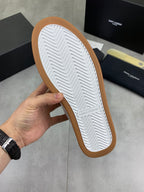 Shoe outsole of white low-top sneakers with gum-brown edge and chevron tread