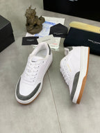 Unisex low-top sneakers: white leather, gray accents, gum outsole, angled side view.